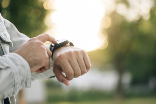 Close up shot of male's hand uses of wearable smart watch at outdoor in sunset. Smart watch. Smart watch on a man's hand outdoor. Man's hand touching a smartwatch.