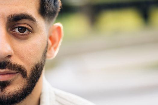 Half face portrait of young man with beard. Half face of upset bearded caucasian young man looking straight to camera while standing outdoors in empty town.