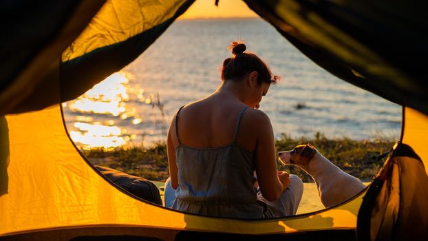 Woman and dog in a tourist tent at sunset. Camping with a pet.