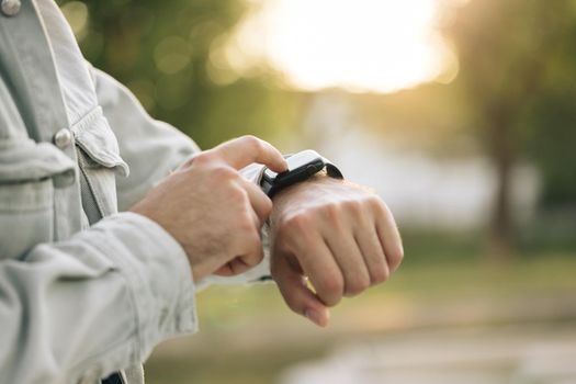 Man's hand touching a smartwatch. Close up shot of male's hand uses of wearable smart watch at outdoor in sunset. Smart watch. Smart watch on a man's hand outdoor.