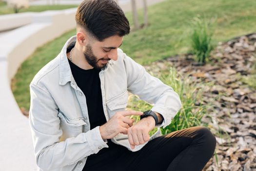 Bearded mixed-race elegant man touching a smartwatch. Male uses of wearable smart watch at outdoor in sunset. Smart watch on a man's hand outdoor. Smart watch.