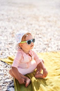 Little girl in sunglasses sits on the beach. High quality photo
