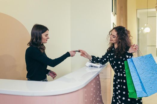 Calculation in the grocery store. Young beautiful woman pays by credit card for her purchases. Gives a credit card to the cashier. The seller gives the woman paper bags with the goods. Standing at the counter in the store in the mall