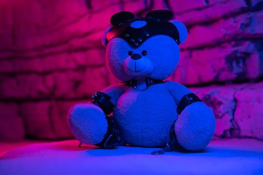 a toy teddy bear dressed in leather belts and a mask, an accessory for BDSM games on a background of rocks texture