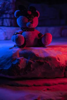 a toy teddy bear dressed in leather belts and a mask, an accessory for BDSM games on a background of rocks texture