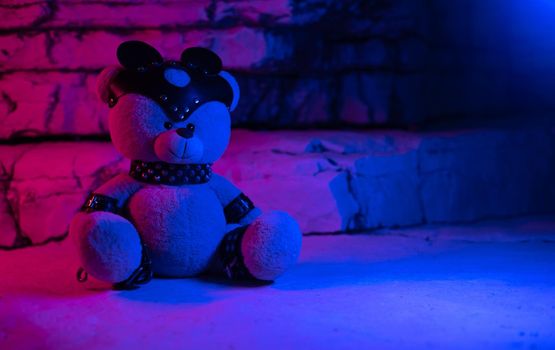 a toy teddy bear dressed in leather belts and a mask, an accessory for BDSM games on a background of rocks texture