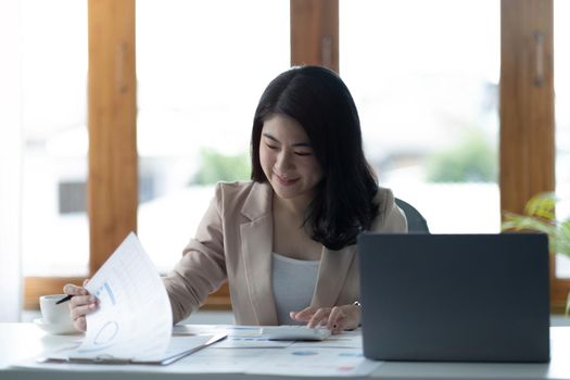 Asian Businesswoman using a calculator and laptop computer for doing math finance on a wooden desk, tax, accounting, statistics report and analytical research concept..