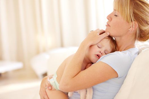 Beautiful woman cradling her sleeping baby to her chest on the couch at home.