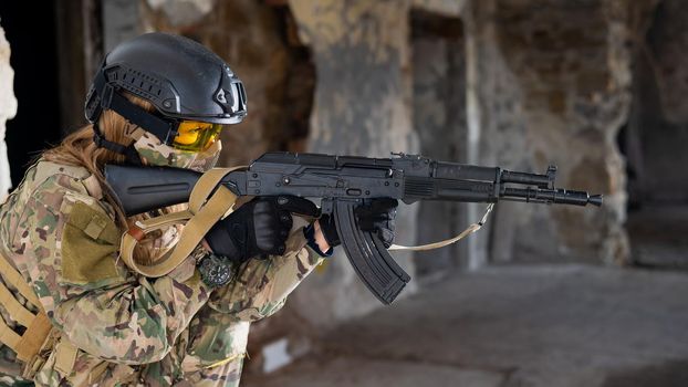 Portrait of a woman in a helmet and goggles with a machine gun in her hands. A female soldier in a camouflage uniform holds a weapon