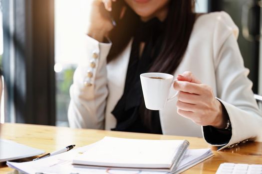 young Asian businesswoman drinking coffee and talking on the phone while working.