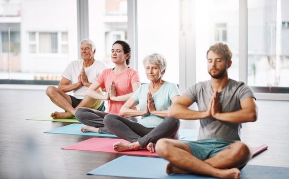 Full length shot of a group of people meditating while practicing yoga.