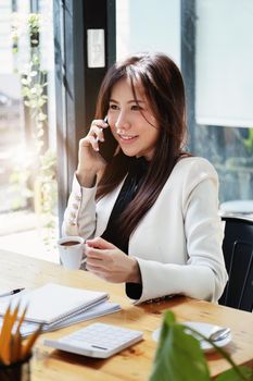 Portrait of a young Asian businesswoman drinking coffee and talking on the phone while working.