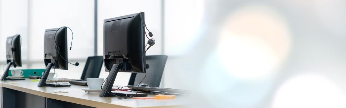 Call center computers and headsets all in office in widen view. Telemarketing, customer support agent provide service on telephone video conference call.