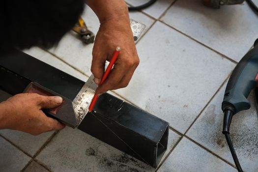 The technician is using a ruler to measure right angles and then use a pencil to mark the precision in cutting steel.