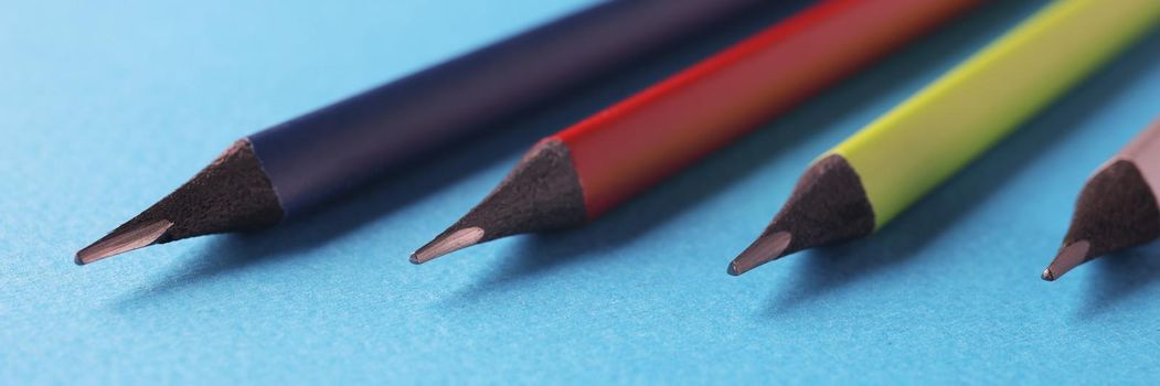 Close-up of colored pencils arranged in decreasing size order on blue surface. Equipment for drawing your dreams, ideas and vision. Art, creativity concept