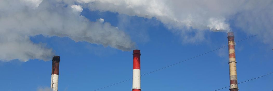 Close-up of smoking pipes of heating plant supplying heat to city, power station with three smoke stacks. Air pollution, ecology and production concept