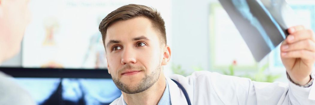 Portrait of smiling doctor talking with patient about good x ray results. Doc looking at visitor with happiness. Recovery, medical and healthcare concept