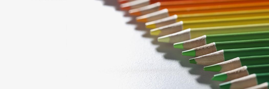Close-up of colourful pencils set perfectly arranged in line on white surface. Macro of crayons ready for drawing picture. Creativity, vision, art concept