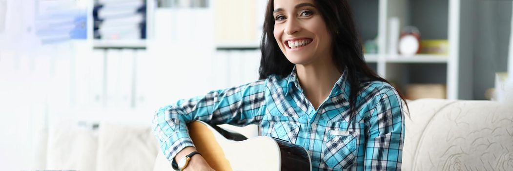 Portrait of happy young woman playing on guitar in living room at home, spend free time learning new song on musical instrument. Music, hobby, joy concept