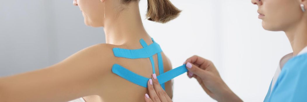 Portrait of doctor apply kinesiology tape on patient back in clinic. Procedure on recovering after injury. Rehabilitation room, healthcare, therapy concept