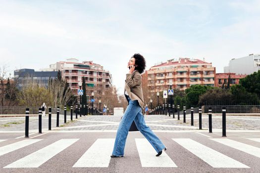 smiling business woman walking on a crosswalk talking by mobile phone, concept of communication and urban lifestyle, copy space for text