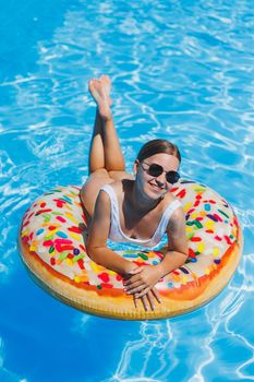 Rest in the pool. Happy young woman in swimsuit, sunglasses and inflatable rubber ring floating in blue water. Summer luxury holidays in the spa resort pool