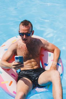 An attractive man is relaxing on an inflatable ring in the pool. A man in the pool is talking on the phone. vacation and free time concept