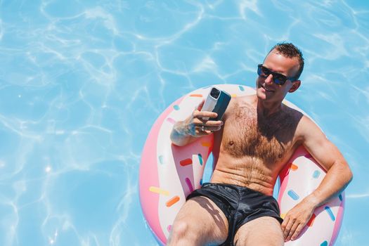 An attractive man is relaxing on an inflatable ring in the pool. A man in the pool is talking on the phone. vacation and free time concept