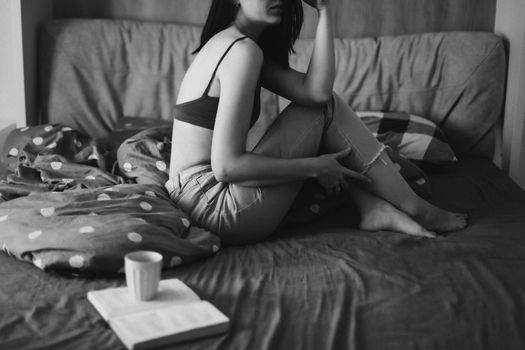 Young sexy woman portrait in bed with a book and coffee cup in the morning