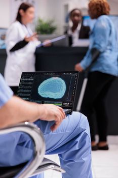 Male nurse analyzing brain animation on laptop, sitting in waiting room hospital lobby. Looking at neurology illustration of vital organ on computer display at healthcare clinic.