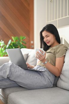 Beautiful asian woman sitting on couch and using laptop, remote working from home or spending time in social media.