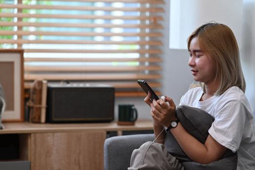 Smiling young woman siting on couch and using smart phone.