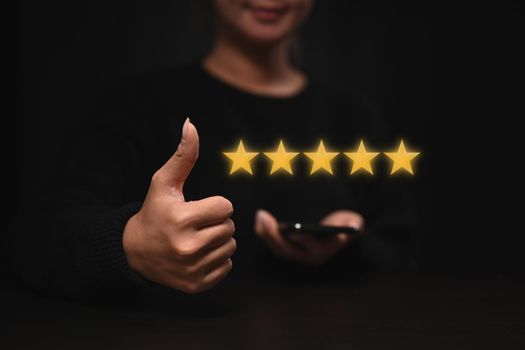 Happy young woman showing thumb up with gold five star icon for giving best score point to review.