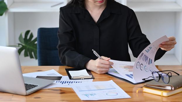 Cropped shot thoughtful businesswoman checking financial reports on office desk.