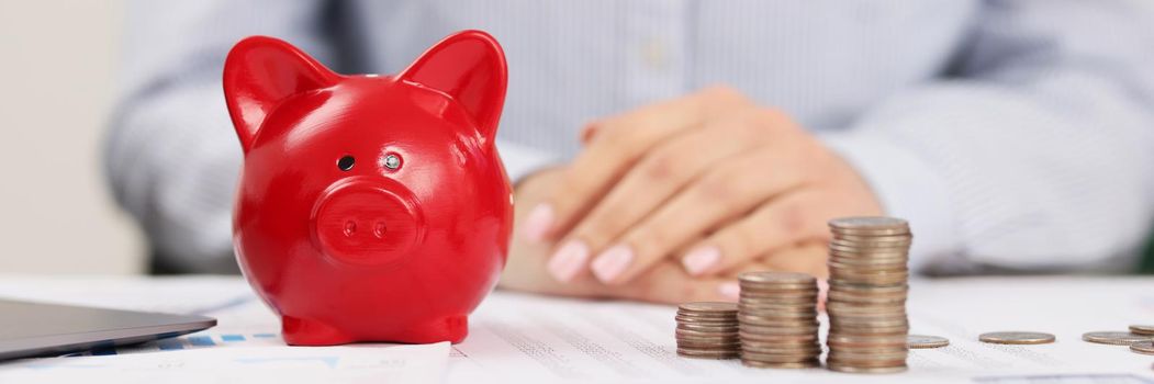 Close-up of person accountant on working place, stack of coins, red piggy bank. Prepare annual report for company on finance. Economy, saving up concept