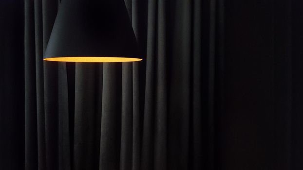 Close-up on a modern lamp against the background of the folds of curtains in dark colors with copy space.