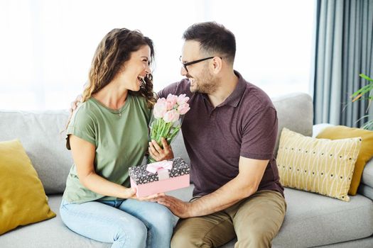 Smiling woman and boyfriend for giving her a present at home