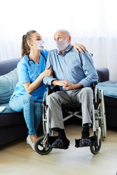 Doctor or nurse caregiver with senior man in a wheelchair wearing protective masks at home or nursing home