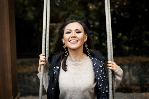 Portrait of young smiling woman sitting on swing in forest. High quality photo