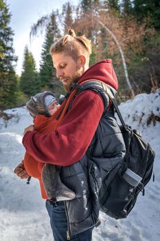 Little boy sleeping in his father's sling while walking in the winter forest.