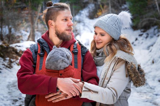 Portrait of young babywearing family with his son in baby carrier winter outdoor.
