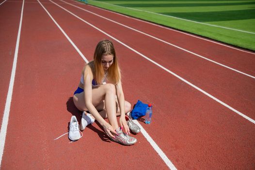 Young caucasian woman tying shoelace before jogging at stadium