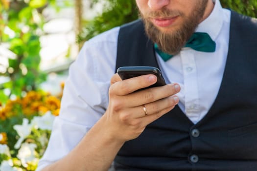 Close-up on a smartphone in the hand of a bearded hipster in a suit, summer outdoor.