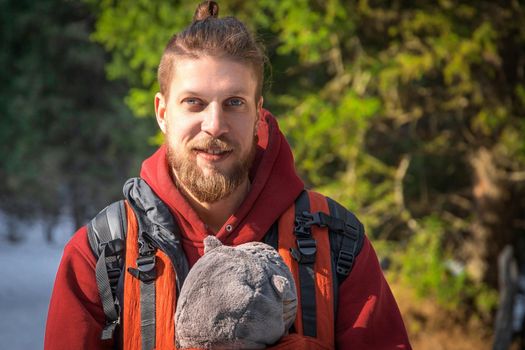 Portrait of bearded babywearing father with his son in baby carrier, family winter hiking.