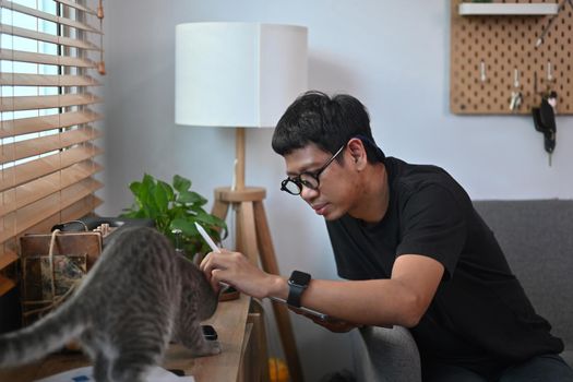 Young asian man playing with his cute cat in living room.