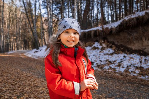 Joyful smiling happy preschool aged girl in red jacket in deep fall forest.