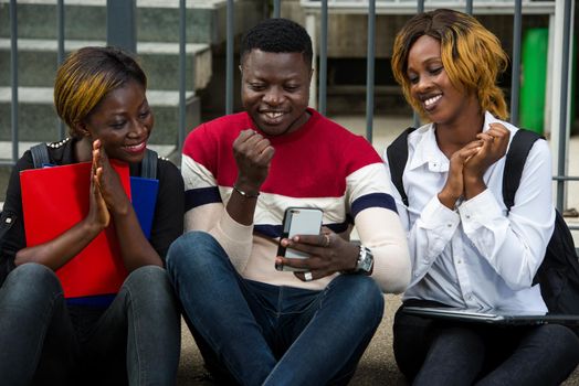 students sitting on the floor looking at mobile phone smiling.