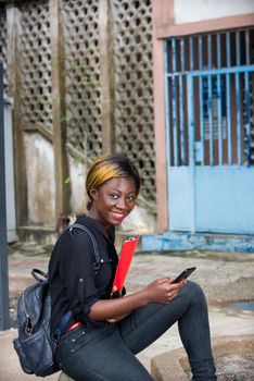young student sitting with mobile phone watching the camera smiling.