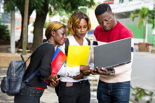 Students standing in the street after classes looking at laptop.