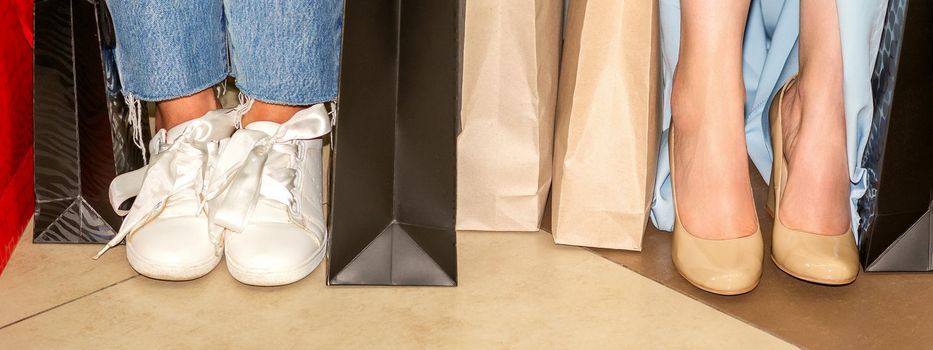 Beautiful feet of two young women with shopping bags after shopping in the mall